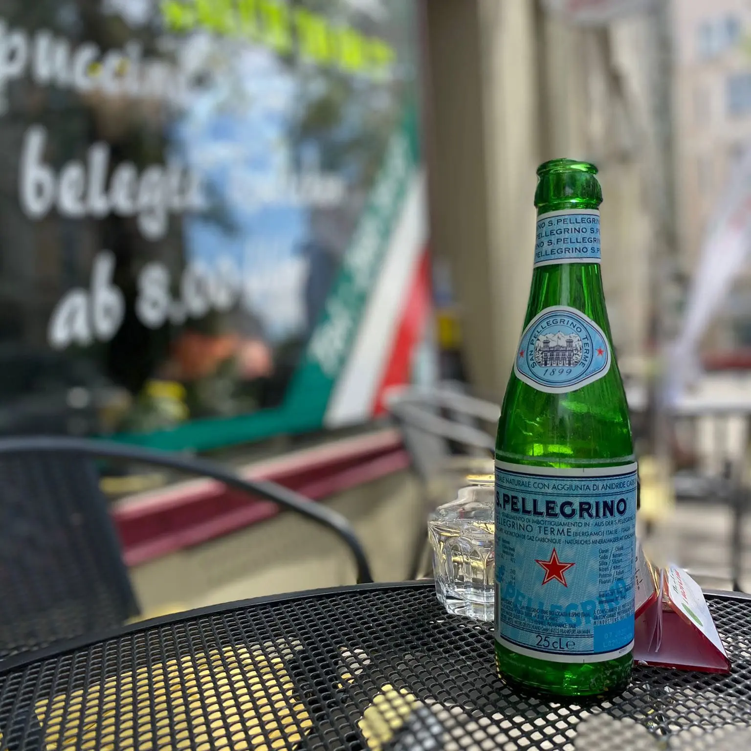 Ein Glas mit einer Flasche Pellegrino auf einem Tisch vor der Pasteria